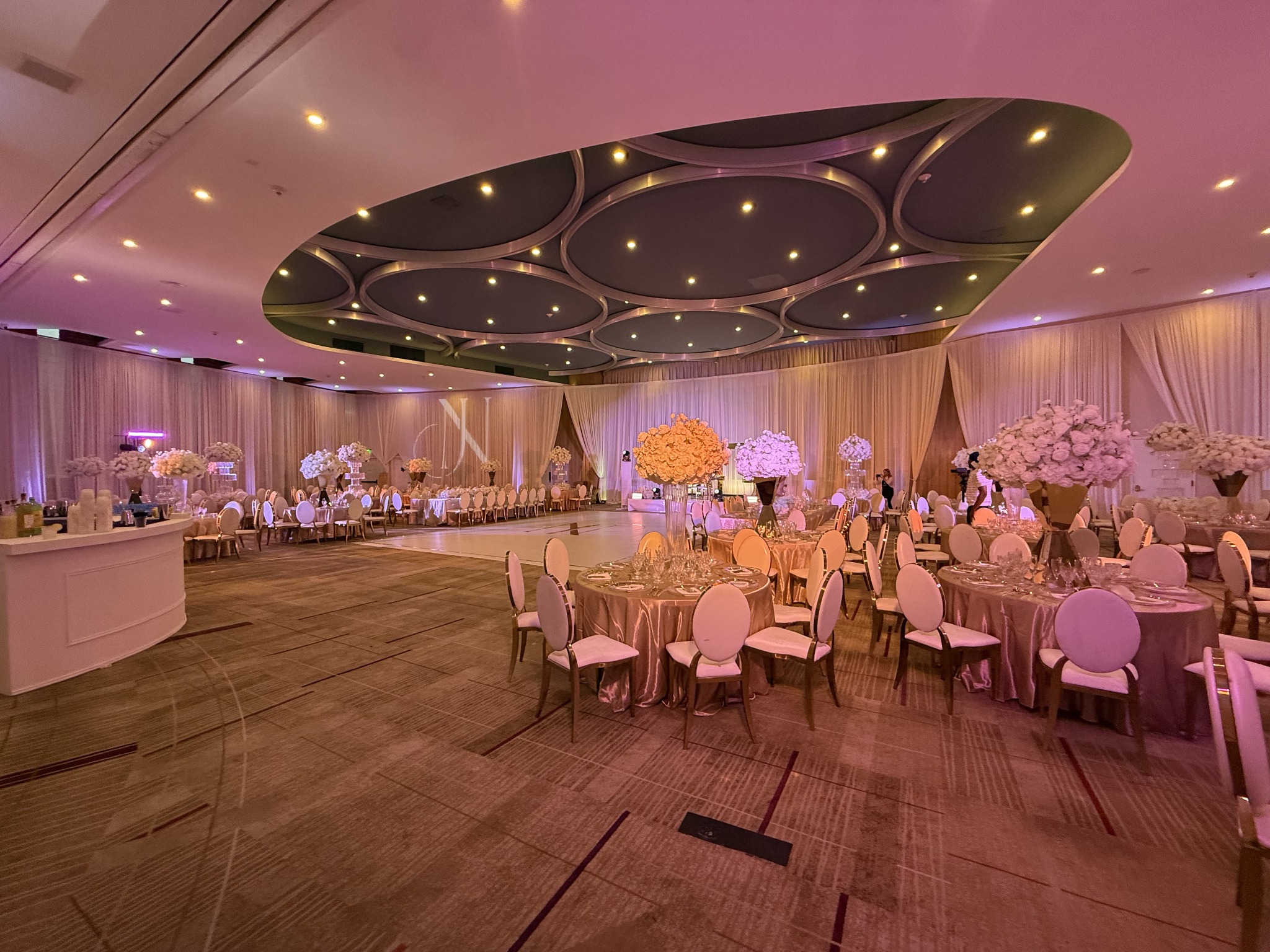 Large wedding ballroom with draped walls, lit floral centerpieces, and a dance floor